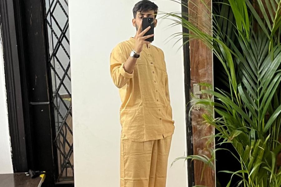 A male customer wearing a beige gold silk loungewear set, taking a mirror selfie indoors.