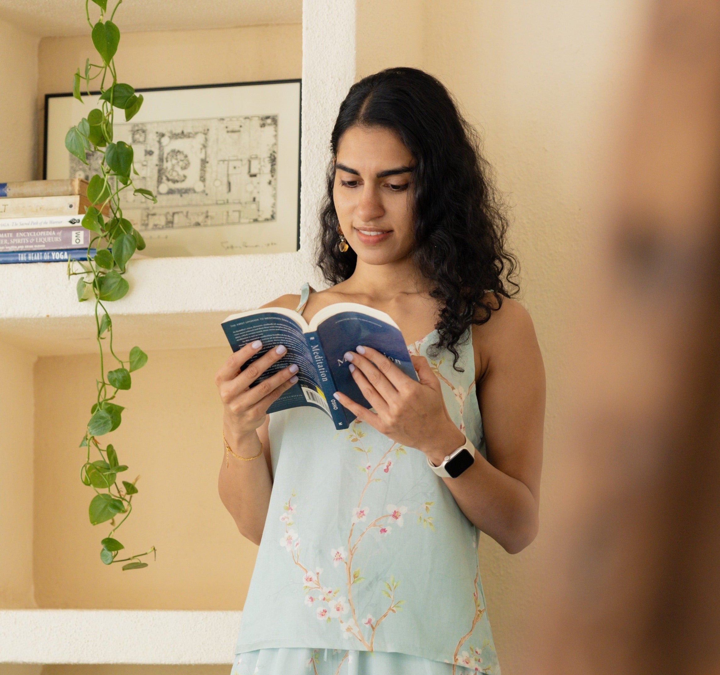 Paizlie customer wearing a beautiful floral dreams lounge wear,  reading a book in a room with shelves and plants